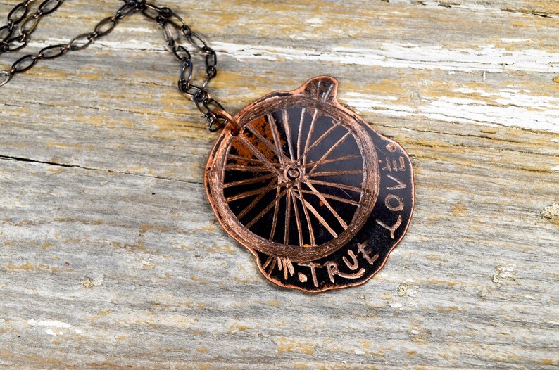 May include: A copper necklace with a black wheel design pendant. The pendant has the words "True Love" inscribed around the wheel.