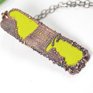 May include: A lime green enamel pendant with a textured copper frame. The pendant is attached to a silver chain.