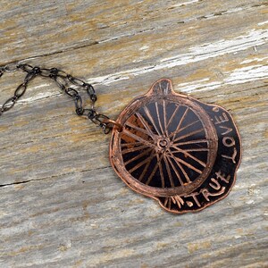 May include: A copper necklace with a black and copper wheel pendant. The pendant is inscribed with the words "True Love".