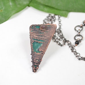 May include: A copper and green pendant necklace with a textured, geometric design. The necklace features a black onyx bead and a silver chain.