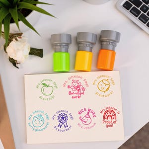 May include: Three colorful stamps with gray tops and green, yellow, and orange bases. Below are stamped images with phrases like "Great Job!" and "Bee-utiful work!" The stamps are for Mrs. Johnson.