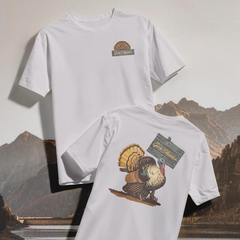 May include: Two white t-shirts. One shirt has a small graphic on the front with the text "Give Thanks". The other shirt has a large turkey graphic on the back, holding a sign that says "Give Thanks".