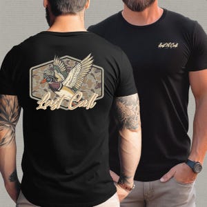 May include: Black t-shirts with a duck graphic. One shirt features a large design on the back with a duck in flight, camouflage background, and the text "Last Call." The other shirt has a smaller logo on the chest.