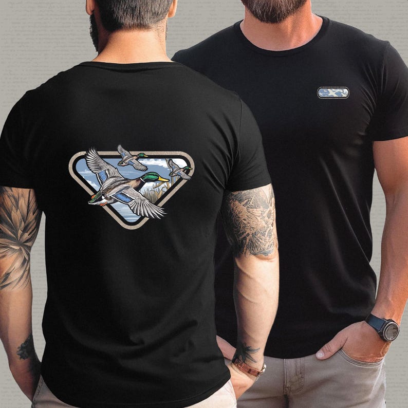 May include: Black t-shirts with a duck graphic. One shirt features a triangular design with flying ducks over a lake. The other shirt has a small rectangular design on the chest. Both shirts are short-sleeved.