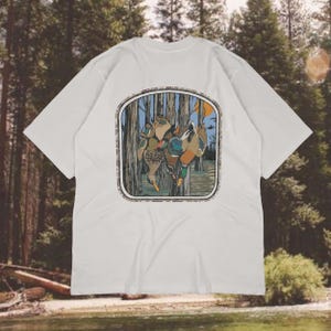 Op de afbeelding: Wit T-shirt met een kleurrijke afbeelding van eenden in een boslandschap, omlijst door een rechthoekige rand. Het shirt heeft korte mouwen en een klassieke ronde hals.