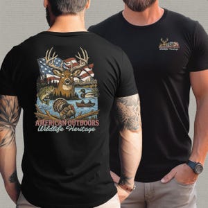 以下が含まれることがあります： 黒いTシャツ。鹿、アメリカ国旗、野生生物のシーンのグラフィックが特徴です。「AMERICAN OUTDOORS WILDLIFE HERITAGE」の文字が下に表示されています。グラフィックの小さなバージョンがシャツの前面にあります。