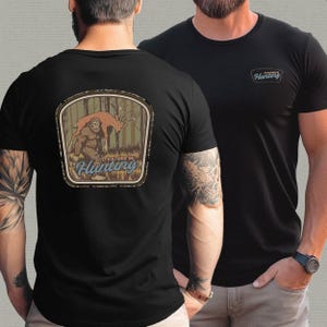 May include: Black t-shirts with a hunting theme. One shirt features a patch with a Bigfoot and deer graphic, the text "I'd Rather Be Hunting". The other shirt has a small patch with the word "Hunting".