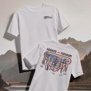 May include: Two white t-shirts. One has a small graphic and the text "HOOKED ON FREEDOM" on the front. The other has a graphic of fishing lures with an American flag design and the text "HOOKED ON FREEDOM" on the back.