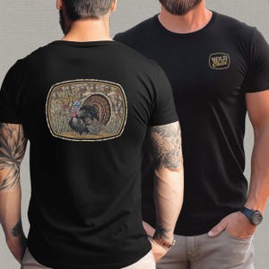 May include: Black t-shirts with a "Wild Child" logo. One shirt features a turkey graphic on the back within a rectangular frame. The other shirt has the logo on the front. The turkey graphic includes a colorful turkey with a fanned tail.