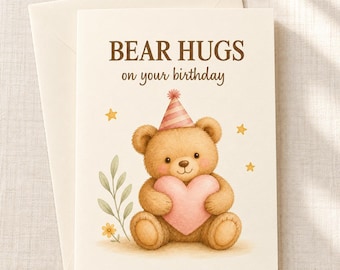Puede incluir: Una tarjeta de felicitación de cumpleaños color crema con sobre a juego. La tarjeta muestra un oso de peluche marrón con un gorro de fiesta a rayas rosas, sosteniendo un gran corazón rosa. El texto dice BEAR HUGS on your birthday con estrellas.
