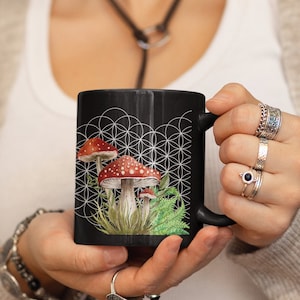 May include: Black ceramic mug with a white geometric pattern and a watercolor illustration of red and white mushrooms with green foliage.