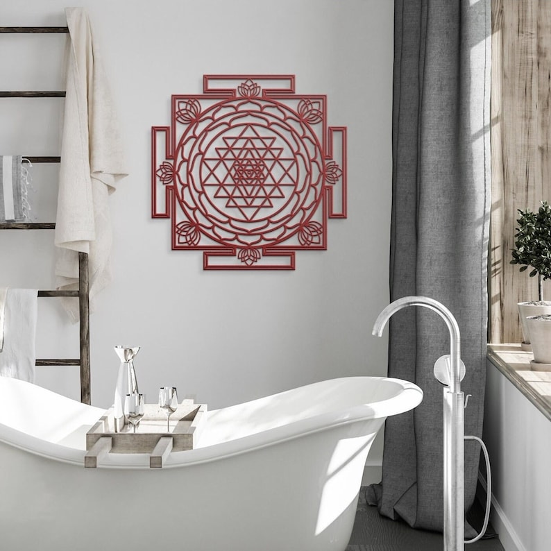 May include: A red metal wall art piece featuring a Sri Yantra design. The design is intricate and detailed, with a central triangle surrounded by a series of concentric circles and triangles.