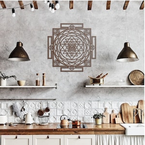 May include: A brown wooden wall hanging with a geometric design, featuring a mandala with a central pyramid shape. The wall hanging is displayed in a kitchen setting with white tile backsplash and wooden countertops.