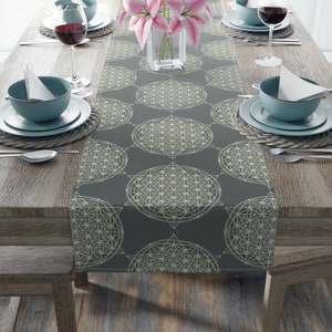 Könnte beinhalten: Ein grauer Tischläufer mit einem geometrischen Muster aus weißen Kreisen und Sternen. Der Läufer liegt auf einem Holztisch mit Gedecken auf beiden Seiten.