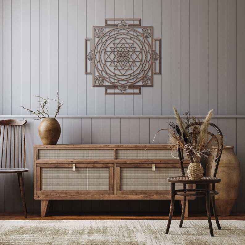 May include: A wooden wall decor with a geometric design in the shape of a square. The design is a brown color and has a intricate pattern. The decor is hanging on a light gray wall.
