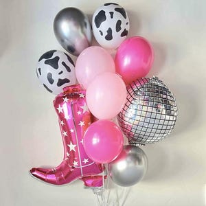 Pode incluir: Um ramo de balões com uma bota de cowboy rosa, balões rosa, prateados e preto e branco com estampa de vaca, e um balão de bola de discoteca prateado.