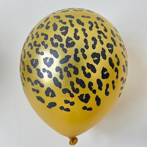 Könnte beinhalten: Ein goldfarbener Ballon mit einem schwarzen Leopardenmuster. Der Ballon ist aufgeblasen und rund, mit einem verknoteten Ende. Der Leopardenprint besteht aus unregelmäßigen schwarzen Flecken auf der Oberfläche. Geeignet für Partys und Feiern.