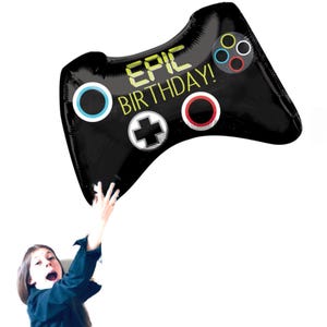 Op de afbeelding: Een zwarte en zilveren folie ballon in de vorm van een videogamecontroller met de tekst "EPIC BIRTHDAY!" in geel.