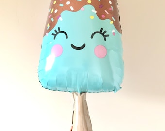 May include: A blue and brown foil balloon shaped like an ice cream popsicle with a smiling face and sprinkles.