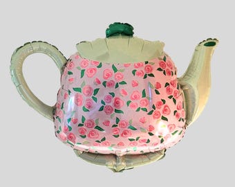 May include: A large, pink teapot-shaped balloon with a floral rose pattern. The balloon has a green lid and handle, and a silver-colored spout and base. The balloon is designed for party decorations.