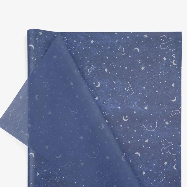 Puede incluir: Papel de regalo azul oscuro con un dise&ntilde;o celestial. Presenta constelaciones, estrellas y lunas crecientes blancas. Una esquina est&aacute; doblada, revelando una capa transl&uacute;cida azul m&aacute;s clara.