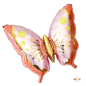Könnte beinhalten: Ein rosa-orangerer Ballon in Form eines Schmetterlings aus Folie mit goldenen Akzenten und gelben Punkten. Der Ballon ist aufgeblasen und bereit für eine Party oder Feier.