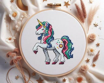 Puede incluir: Un bastidor de bordado de punto de cruz con un diseño de unicornio colorido. El unicornio tiene un cuerno amarillo, una melena y cola multicolores, y una estrella en el flanco. El bordado está en un bastidor de madera, rodeado de estrellas y flores decorativas.