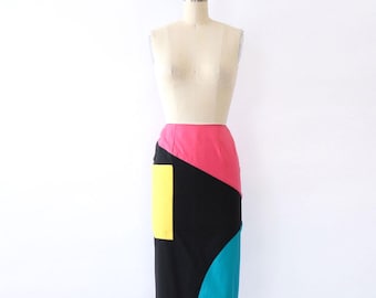 May include: A black, pink, yellow, and blue geometric patterned skirt. The skirt is knee-length and has a fitted silhouette.