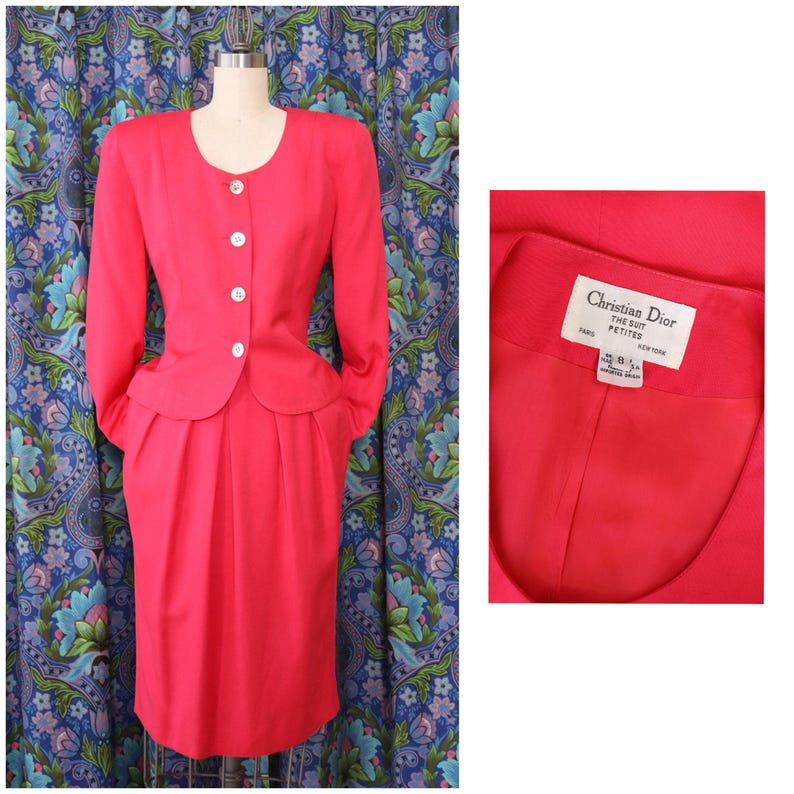 May include: A bright pink Christian Dior suit, featuring a long-sleeved jacket with a rounded collar and three white buttons. The matching skirt is knee-length. The suit is displayed on a mannequin. A close-up shows the label.