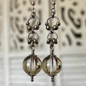 May include: Silver dangle earrings with two silver rings and a clear glass sphere at the bottom.