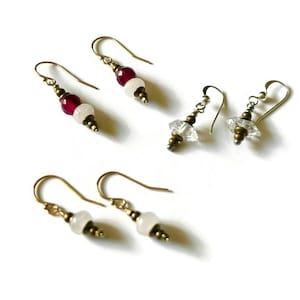 May include: Several pairs of handmade earrings with gold-colored hooks. Some earrings feature red and white beads, while others have clear, faceted crystal-like beads. The earrings are displayed on a white background.