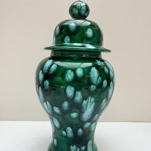 May include: A green ceramic ginger jar with a lid. The jar has a glossy finish with a pattern of teal and dark green spots. The jar is a decorative item.