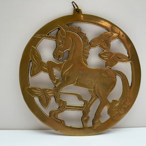 Peut inclure: Décoration murale circulaire en laiton représentant une licorne. La licorne est représentée de profil, dans un cadre circulaire avec des découpes décoratives. Elle possède une boucle pour être suspendue.