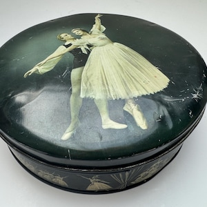 May include: Circular, dark green tin featuring a ballet dancer design on the lid. The lid depicts a dancing couple, the male dancer in black and the female in a white tutu. The tin's sides are decorated with a ballet-themed pattern.