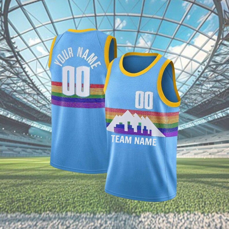 May include: Two light blue basketball vests with yellow trim and rainbow stripes. One vest has "YOUR NAME" and "00" on the back. The other has "TEAM NAME" and a mountain graphic. Both vests are on a green field.
