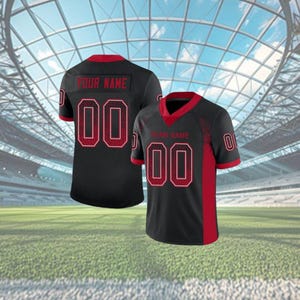 Puede incluir: Camiseta de f&uacute;tbol negra y roja con el n&uacute;mero "00" en la parte delantera y trasera. La camiseta tiene cuello rojo y detalles rojos en las mangas. El texto "YOUR NAME" est&aacute; encima del n&uacute;mero en la espalda.