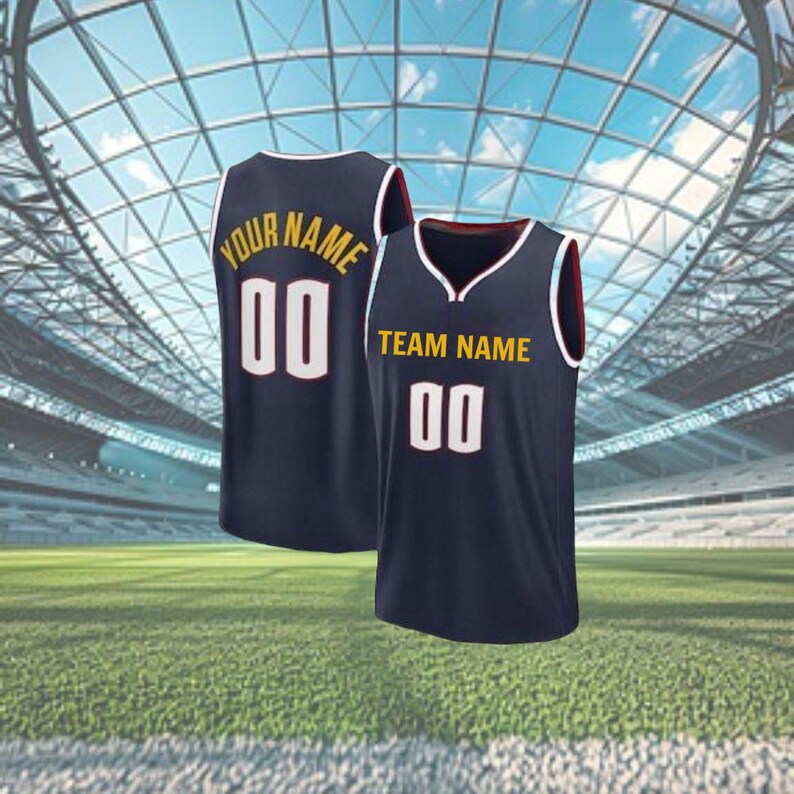 May include: Two navy blue basketball vests with white and gold lettering and numbers. One vest reads "YOUR NAME" and "00", the other reads "TEAM NAME" and "00". The vests have white trim and are set against a stadium background.