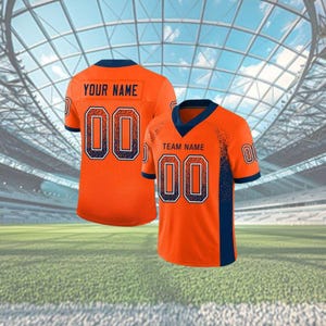 Puede incluir: Dos camisetas de f&uacute;tbol naranja con detalles azul marino. Una camiseta muestra "YOUR NAME" y el n&uacute;mero "00". La otra muestra "TEAM NAME" y el n&uacute;mero "00". Ambas camisetas tienen una textura de malla y est&aacute;n sobre un fondo de estadio.