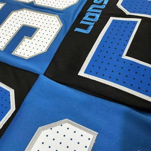 Puede incluir: Primer plano de camisetas deportivas azules y negras. Las camisetas presentan grandes n&uacute;meros blancos con un patr&oacute;n de puntos y ribetes plateados. La palabra "Lions" es visible en letras azules en una camiseta negra.