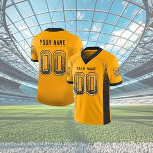 Puede incluir: Dos camisetas de f&uacute;tbol amarillas con detalles negros. Una muestra "YOUR NAME" y el n&uacute;mero "00". La otra muestra "TEAM NAME" y el n&uacute;mero "00". Las camisetas tienen cuellos y mangas negros.