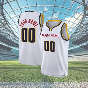 May include: Two white basketball vests with the number "00" in navy blue and gold trim. One vest has "YOUR NAME" in red, the other has "TEAM NAME" in red. The vests are displayed against a stadium background.