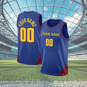 May include: Two blue basketball jerseys with gold lettering and numbers. One jersey has "YOUR NAME" above the number "00" on the back. The other jersey has "TEAM NAME" above the number "00" on the front. Both jerseys have red accents.