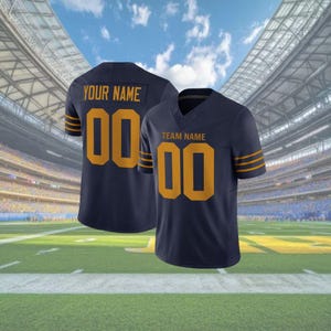Puede incluir: Camiseta de f&uacute;tbol azul marino con detalles dorados. La camiseta muestra el n&uacute;mero "00" en dorado en la parte delantera y trasera, con "TEAM NAME" y "YOUR NAME" encima de los n&uacute;meros. Rayas doradas adornan las mangas. El fondo muestra un estadio.