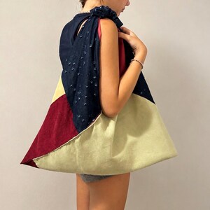 Può includere: Una grande borsa a spalla in stile hobo caratterizzata da un design a blocchi di colore con pannelli in tessuto blu navy testurizzato, velluto a coste bordeaux scuro e velluto a coste verde salvia chiaro. La borsa ha una tracolla ampia arricciata.