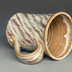 May include: A handmade ceramic mug with a white and brown glaze. The mug has a unique swirl pattern and a large handle.