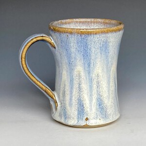 May include: A handmade ceramic mug with a light blue glaze and a brown rim. The mug has a flared shape and a handle.