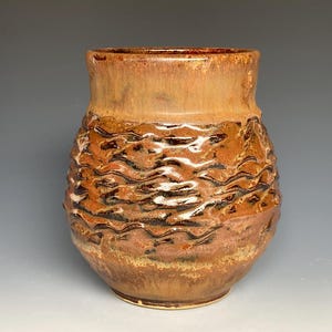 May include: A brown ceramic vase with a textured, wavy design. The vase has a wide mouth and a rounded body.