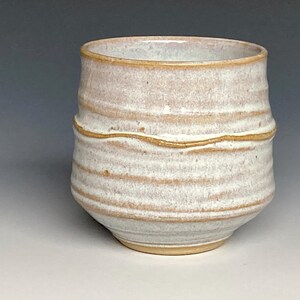 May include: A white ceramic mug with brown stripes and a slightly flared rim.