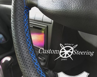 Può includere: Primo piano di un volante in pelle nera con cuciture blu. Il volante ha un design traforato e il testo "Custom Steering" e "Genuine Leather" è visibile.