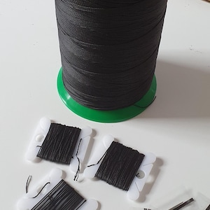 May include: A large spool of black nylon thread with a green base and the brand name "oman". Several small spools of black thread and needles are also present, ideal for sewing and crafting projects.